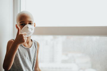 Mask-wearing boy looking outside the window. sick child without hair in the hospital, wears a protective mask and looks out the window. sick boy without hair 