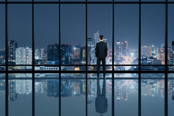 Businessman standing in modern office interior and looking to night city
