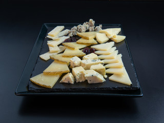 Different types of European cheeses cut in small portions ready to eat, on an elegant black slate plate isolated on a black background.Copy space. Concept of elegance, quality and gourmet food.