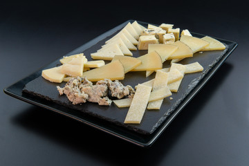 High quality and prestigious European cheeses, cut in small portions and ready to eat, on an elegant black slate plate isolated on a black background. Concept of elegance, quality and gourmet food