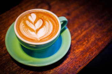 Homemade hot fresh cocoa (coffee or latte) with pattern white milk froth on surface in cup with wooden saucer serve on wooden table, for background - drink concept.