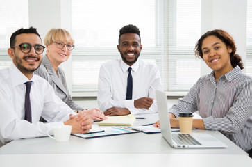 Multy-ethnic group of young business people sitting at the office desk and smiling at camera