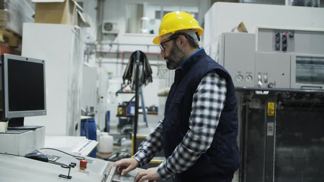 Side view of concentrated male worker setting printing machine. Focused technician working with printing machine. Manufacturing concept