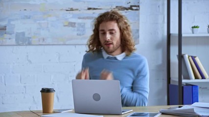 happy curly man dancing near laptop in office