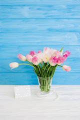 Tulips flowers in glass vase with gift card over blue wooden background for March 8, Women's Day, Birthday, Valentine's Day or Mother's day