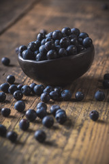 Clay bowl with organic, wild forest blueberries on a rustic wooden table.