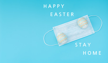 Decorated Easter eggs lie on the medical face mask on blue background with text. Happy Easter during quarantine concept. Biohazard, 2019-nCoV, COVID-19, social distance. Flat lay style with copy space