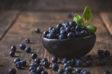Clay bowl with organic, wild forest blueberries on a rustic wooden table.