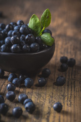 Clay bowl with organic, wild forest blueberries on a rustic wooden table.