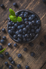 Clay bowl with organic, wild forest blueberries on a rustic wooden table.