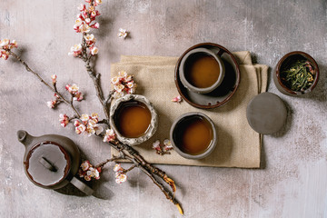 Tea drinking wabi sabi japanese style dark clay cups and teapot on cloth napkin with blooming...