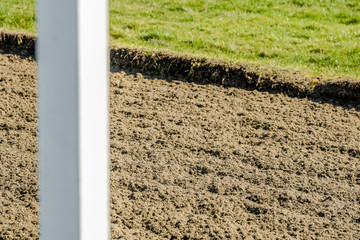 Shallow focus of a newly racked professional horse flat-race track, showing the soft, fibre surface. An out of focus furlong pole is seen in the foreground.