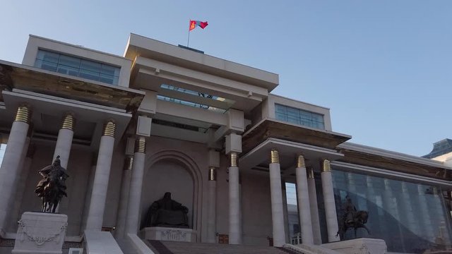 Parliament building in Ulan Bator, Mongolia with statues a side. Flag of Mongolia on top. Camera pan from left to right.