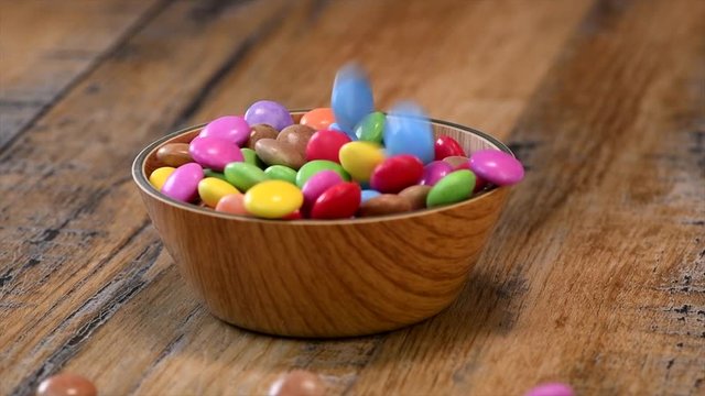 Slow motion, Colorful candies in a wooden bowl case isolated on wood background