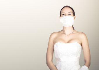 Beautiful young bride in a wedding dress and a white medical mask on face