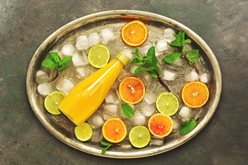 Orange juice in a bottle with slices of citrus, ice and mint leaves. Top view, flat lay.