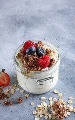 Healthy breakfast. Yogurt in a transparent jar with hercules flakes, granola, fresh raspberries, strawberries and blueberries poured with honey. Background image, copy space