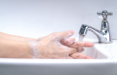 Woman washing hand with soap foam and tap water in bathroom. Hand clean under faucet on sink for...