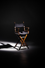 Directors chair stands in the beam of light. Space for text. Vacant chair. The concept of selection and casting. Shadow and light. - obrazy, fototapety, plakaty