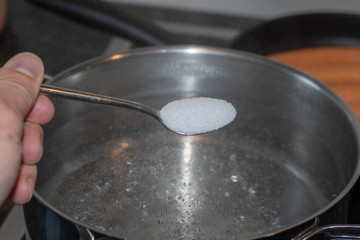 Salz vom Löffel in das kochende Wasser schütten