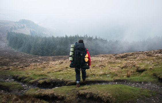 Viajero cargado con mochila grande observando el paisaje en la montaña en un día con niebla