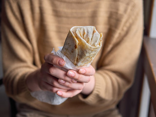 Close Up no face detail shot of woman in yellow sweater holding delicious falafel kebab roll indoors with natural window light