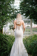 The bride poses showing her back. As the sun goes down, at the wedding venue. The bride is holding a bridal flower in her hand.