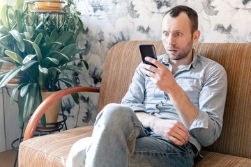 young man with fear reads the news on a smartphone while sitting on a sofa during home isolation during a pandemic coronovirus covid -19