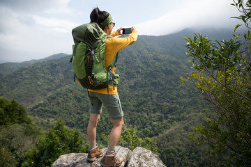 Successful hiker using smartphone on mountain top cliff edge