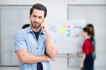 Fototapeta premium Confidence team leader. Young man owner startup business thinking and looking at camera with smile while his colleagues working in the background