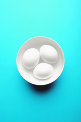 Three white eggs on a vivid aqua blue background. 