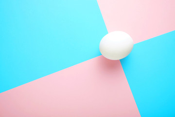 Single white egg on crossing point of blue and ping backgrounds. White egg on a pink-blue background.