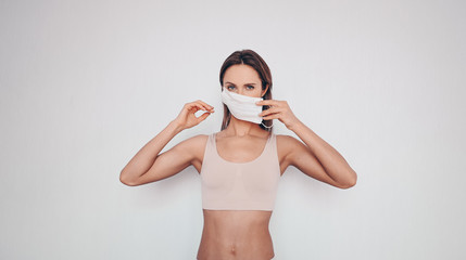 Home fitness. Young fit slim woman in sportswear protection face mask posing during self isolation...