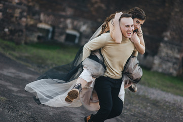 Loving groom in a black cardigan rolls on his back a beautiful bride in an expensive dresses forest...