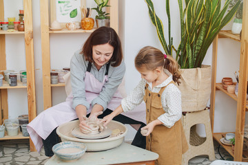 Mom and daughter together, playing with clay make a pot for a potter's
