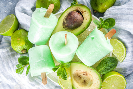 Homemade avocado popsicle. Vegan non-dairy ice cream. Avocado,lime and coconut healthy popsicle on grey stone background with fresh lime slices, avocados and ice