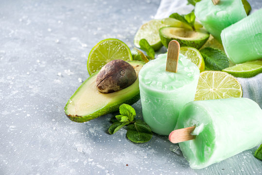 Homemade avocado popsicle. Vegan non-dairy ice cream. Avocado,lime and coconut healthy popsicle on grey stone background with fresh lime slices, avocados and ice