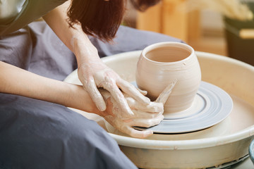 Female hands working with a scraper to remove excess clay from the pot