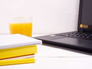 A laptop, a glass of juice, a stack of books and notebooks. The concept of working on the Internet, learning on the Internet.