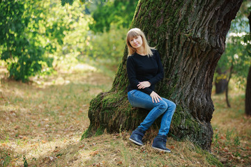portrait a smiling pregnant woman walking in jeans in the park near the tree. beautiful blonde pregnant woman strokes and touches the belly outdoors in sunny day. happy 9 months of Healthy Pregnancy