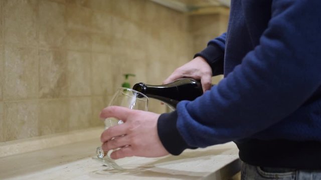A man pours a glass of champagne at home in the kitchen.