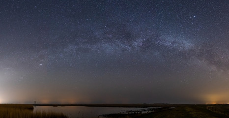 Panaroma shot of the milky way with a moor and reeds in the forground
