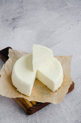 Homemade fresh soft cheese brynza or feta on a wooden cutting board on a gray background. Vertical orientation. Copy space.
