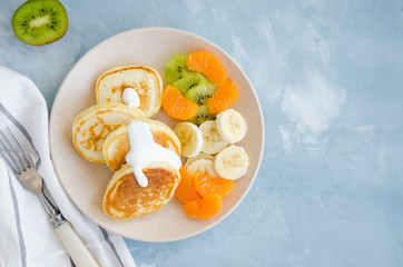 Pancakes on buttermilk or kefir with fresh fruit and yogurt on a plate on a light blue concrete background. A delicious and healthy breakfast. Horizontal orientation. Top view, copy space.