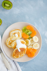 Pancakes on buttermilk or kefir with fresh fruit and yogurt on a plate on a light blue concrete background. A delicious and healthy breakfast. Vertical orientation. Top view, copy space.