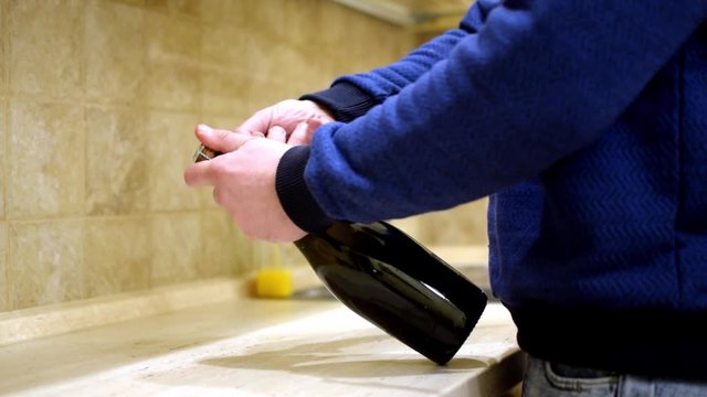 A man opens a bottle of wine at home in the kitchen.