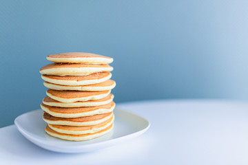 Stack of american pancakes on a white table on blue background. Copyspace. Breakfast and snack