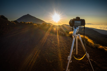 Digital camera on a tripod capturing a sunset in the mountains. Sun rays illuminate the valley.