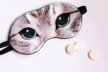 sleep mask with eyes of the cat and pills for sleeping on white background