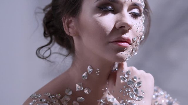 Unusual makeup and face art with sparkling rhinestones on the skin. A girl with precious crystals on her face, a fashion image in light soft colors